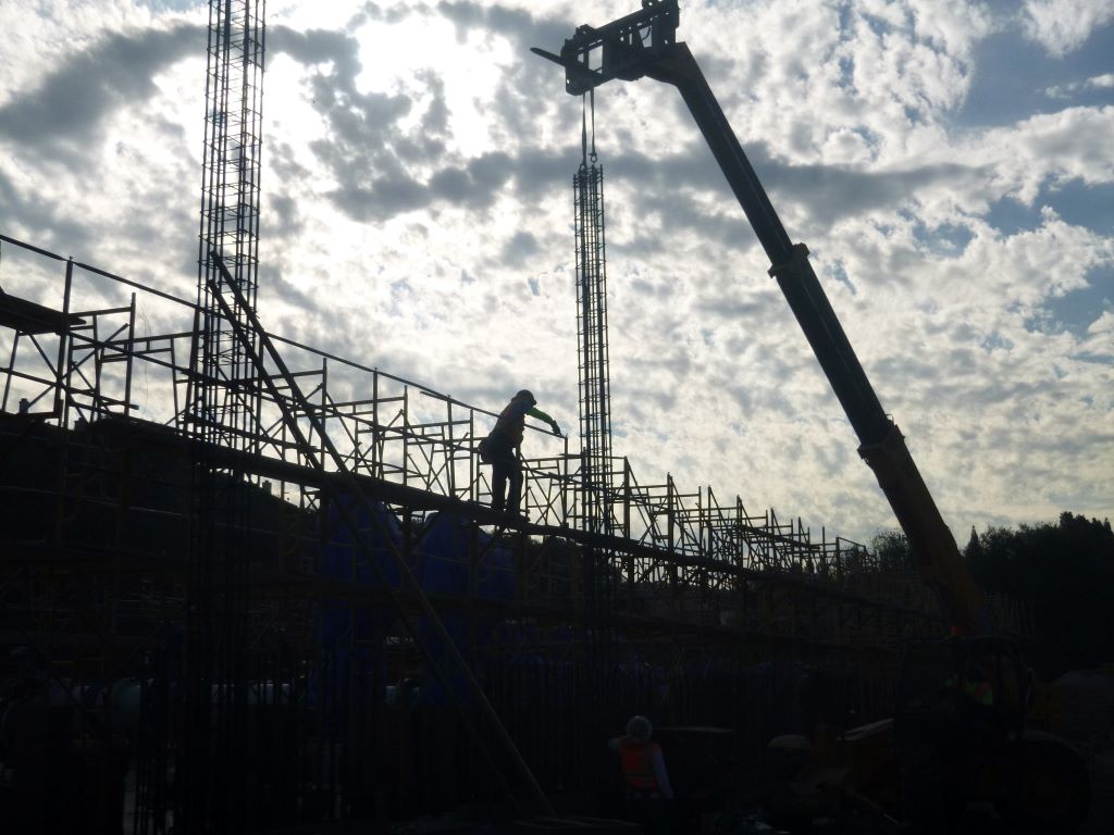 Silhouette of a construction worker, crane, and rebar framing against a cloudy sky.
